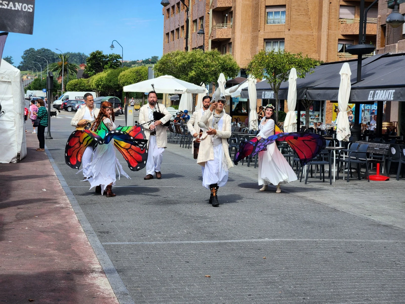Animación de calle con artistas y alas de colores en un evento de Asturias
